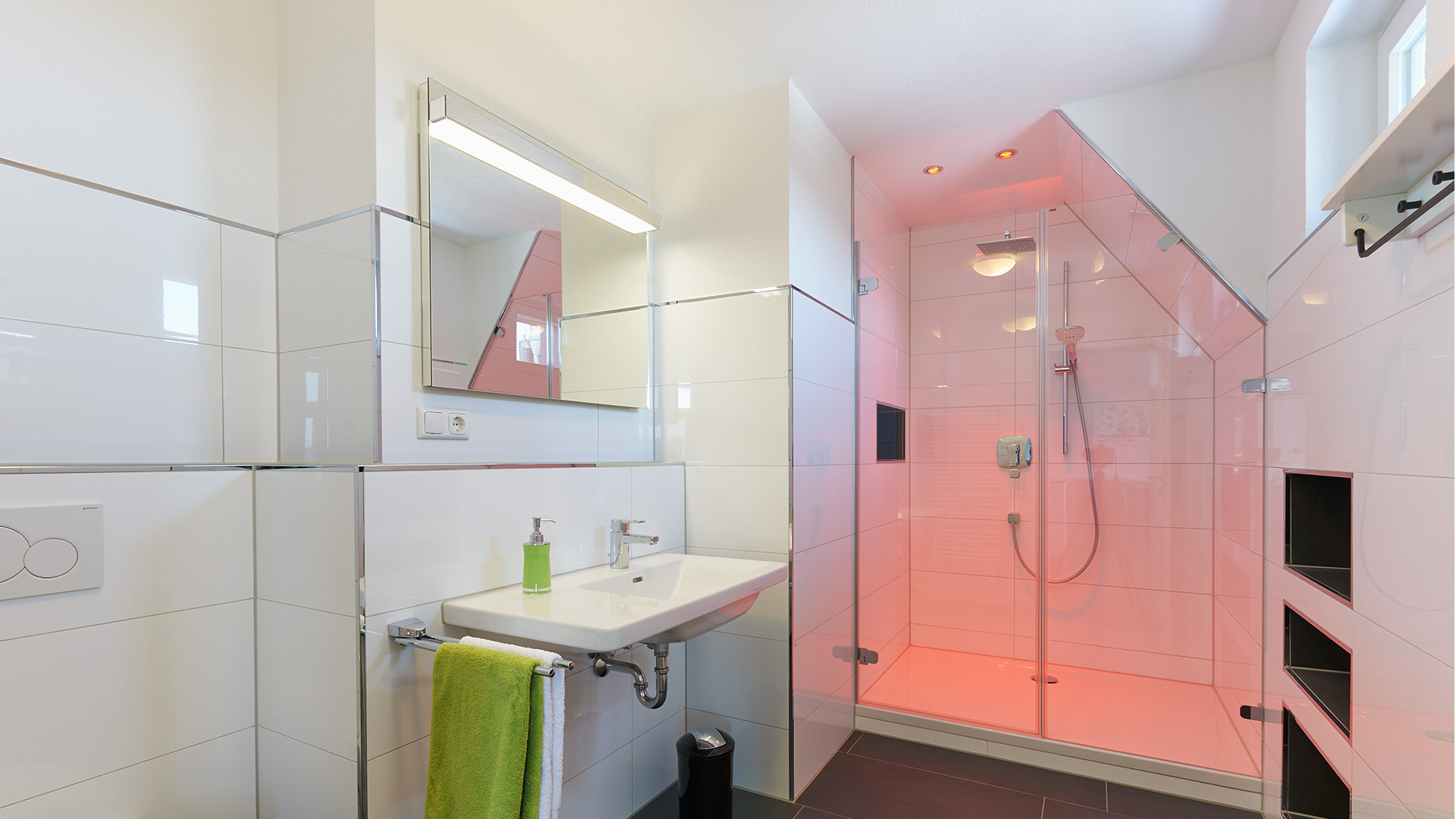 Wechselndes farbiges Licht im Duschbereich bietet einen schönen Kontrast zum reinweißen Badbereich.
