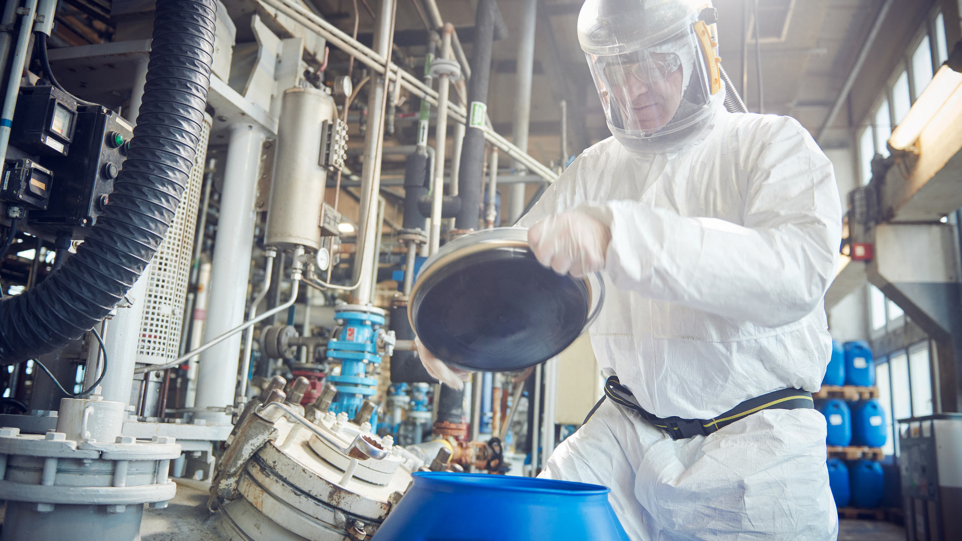 In Arbeitsschutzkleidung und Atemmaske gehülter Produktionsmitarbeiter befüllt einen Behälter. Industriefoto für die Imagekampagne der Organica Feinchemie.